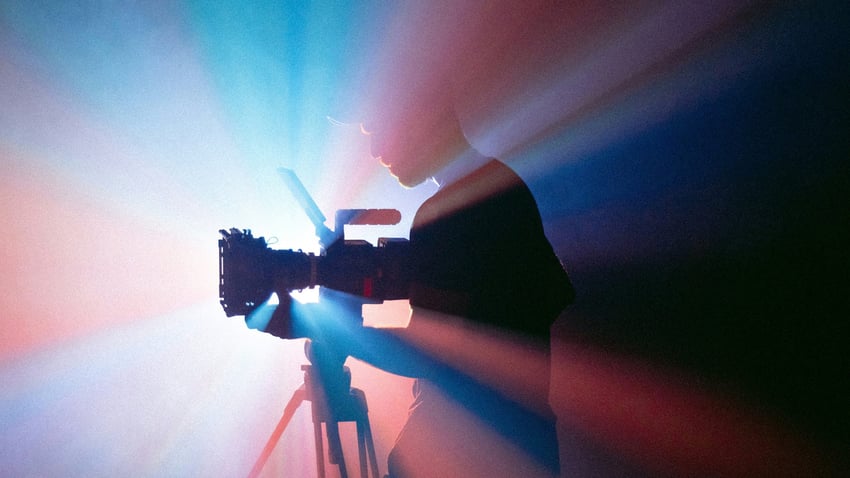 Silhouette eines Kameramanns bei Dreharbeiten mit professioneller Videokamera, dramatische Lichtstrahlen in Blau und Rot