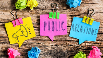 Bunte Notizzettel mit den Worten „Public Relations“ und einem Megafon-Symbol auf Holzuntergrund