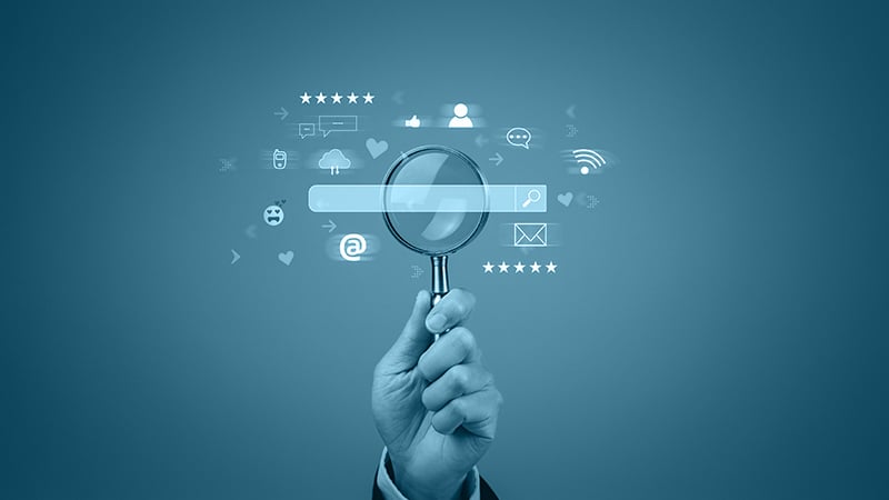 Symbolbild einer Hand mit Lupe vor einer digitalen Suchleiste und Icons – Darstellung von Suchmaschinen und Online-Marketing-Begriffen.